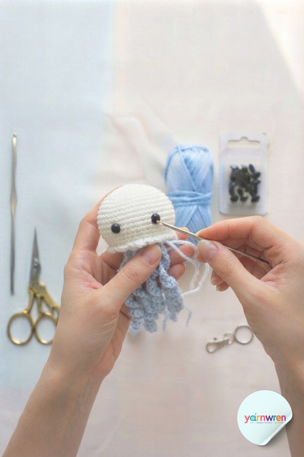Sewing light blue tentacles onto the base of the head in a jellyfish keychain crochet project